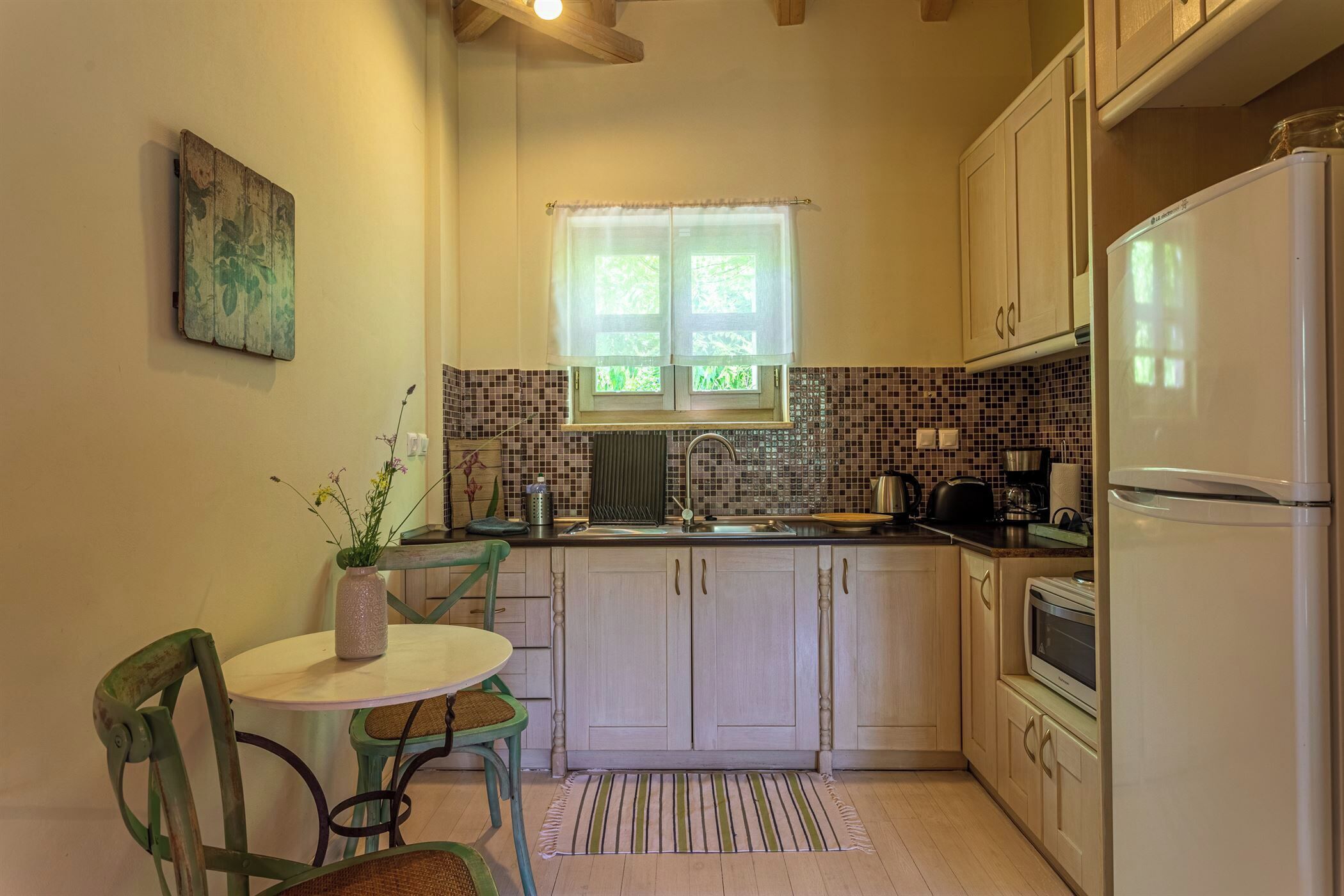 A compact kitchen with a window, a sink, a refrigerator, and a dining area with chairs and a table.