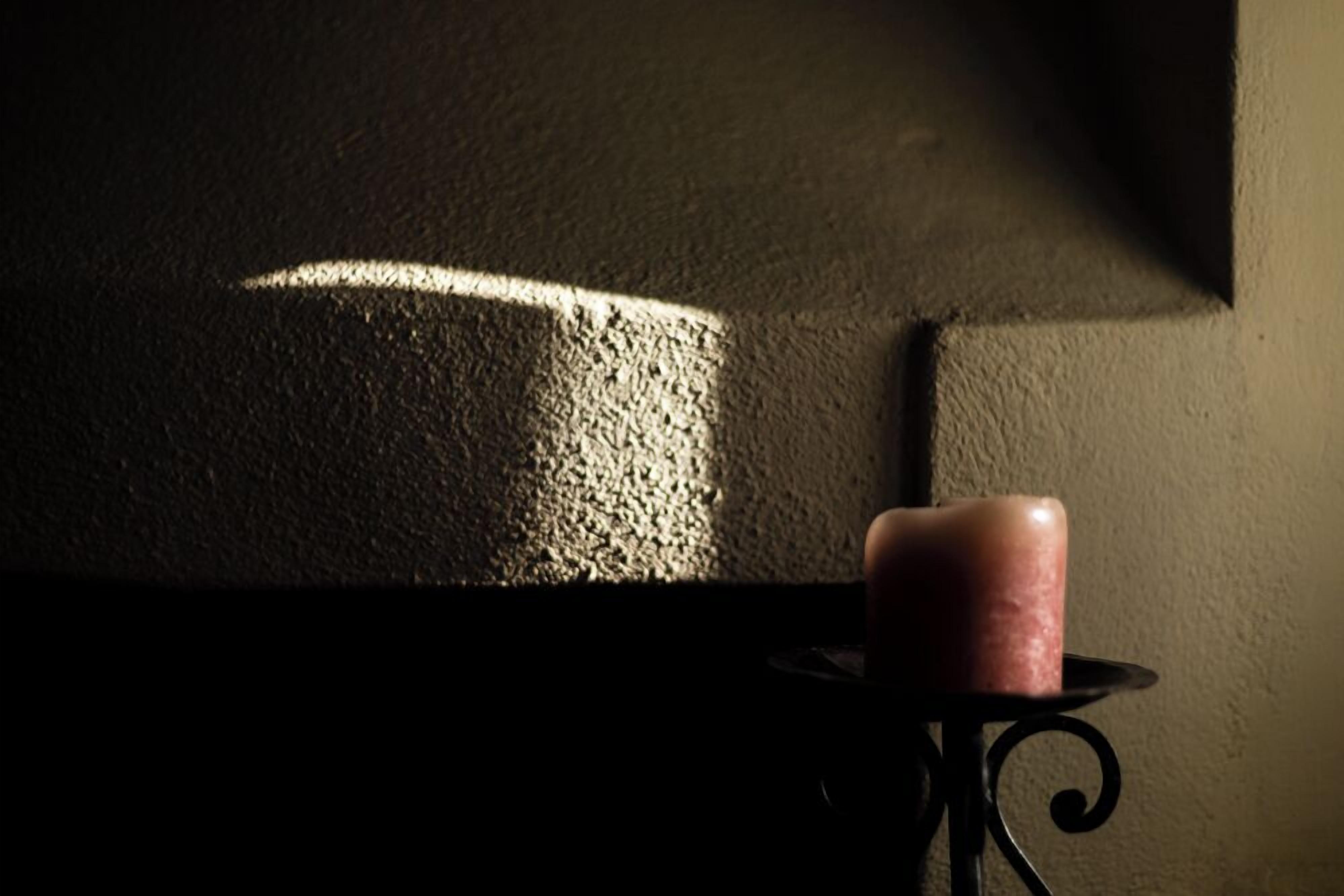 A candle on a small table with a textured wall in the background.