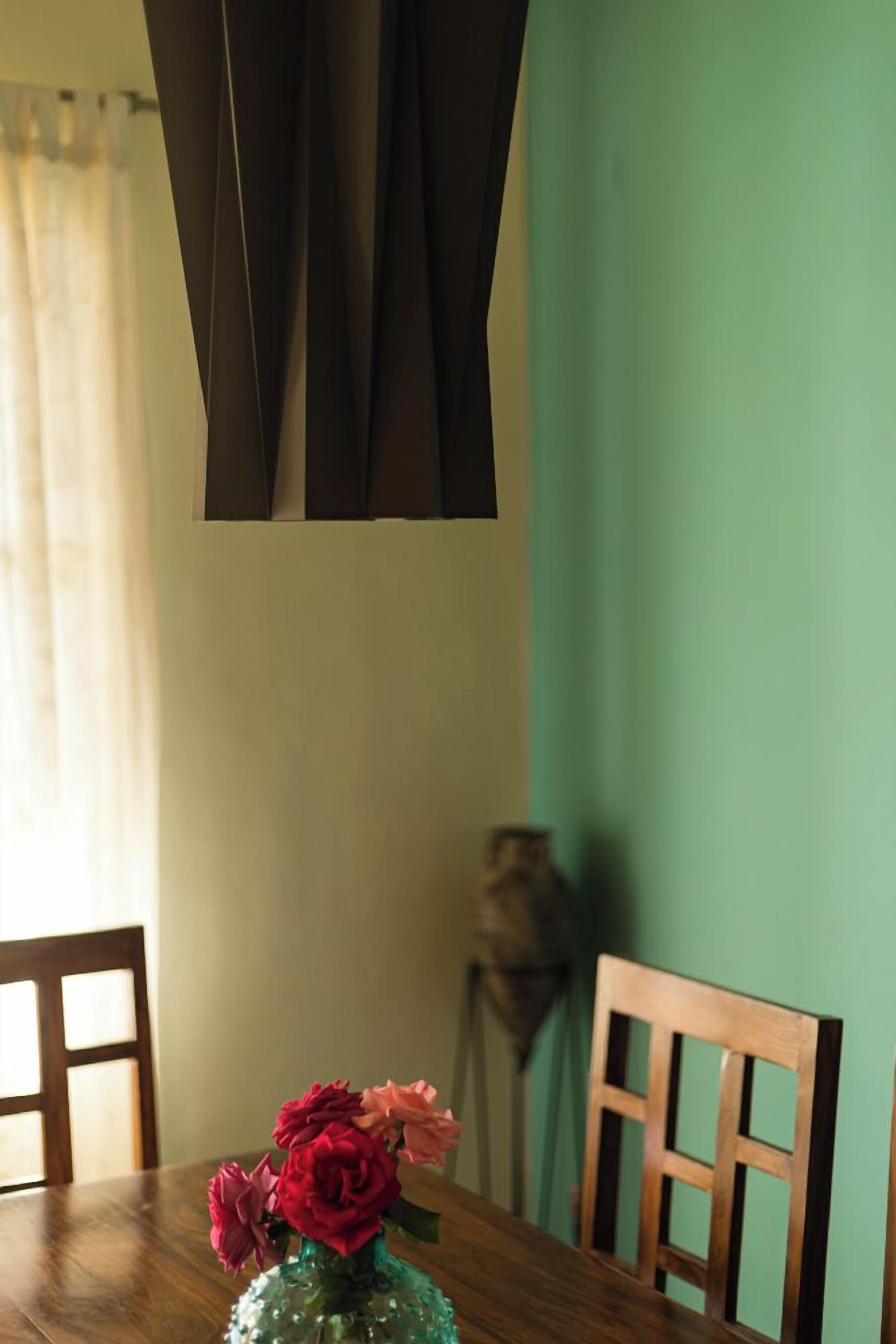 Et spisebord med en vase blomster, træstole og en grøn væg i baggrunden.