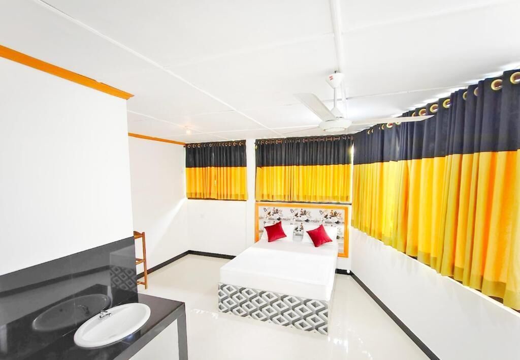 Una habitación de hotel con cama, baño con lavabo y cortinas amarillas.