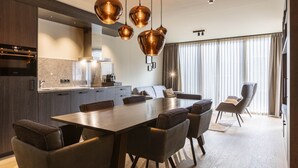 Una cocina moderna con comedor, que presenta un gran mesa de madera, sillas marrón oscuro y lámparas colgantes de cobre.