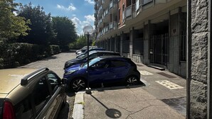 Un espace de stationnement avec des voitures, un immeuble doté de balcons et un ciel dégagé.