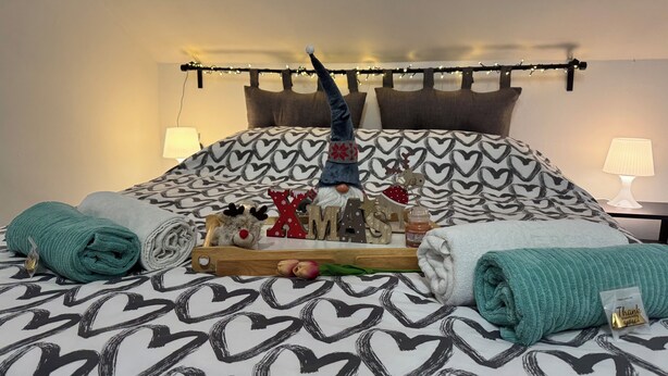 Un lit bien fait, avec une literie à motifs de cœurs, une guirlande décorative et un jouet en peluche.