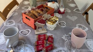 Une table dressée avec une nappe aux motifs de Noël, une décoration représentant un gnome, un signe astrologique et divers aliments.