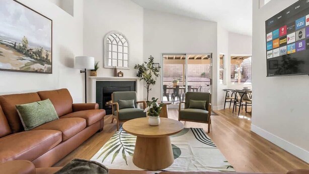 Een moderne woonkamer met een bruine leren bank, groene fauteuils, een houten salontafel en een open haard.