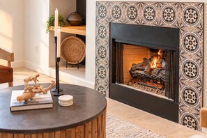 A living room with a fireplace, a round wooden table with decorative items, and a patterned wall.
