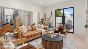 A modern living room with a sofa, coffee table, and chairs. There is a staircase leading to another level, and a large window with a view of the outdoors. - Casa Del Sol Luxe Experience - Walkable 2 Old Town (Paradise Valley)