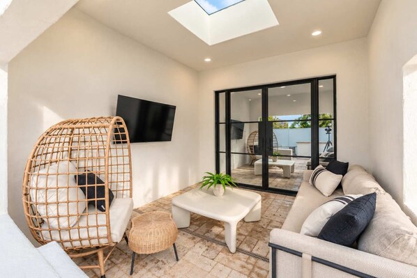 A modern patio with a sofa, a wicker chair, a small table, and a TV mounted on the wall.