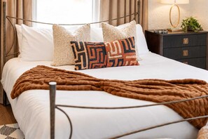 A bed with white bedding, a brown throw blanket, and patterned pillows.
