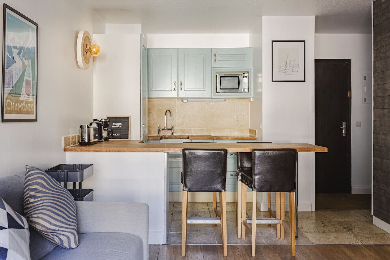 A compact kitchen with a central island, two bar stools, and a coffee machine.