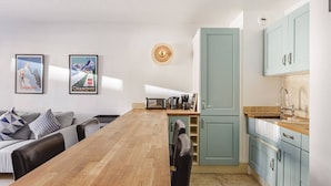 A modern kitchen with light blue cabinets, a wooden dining table, and a coffee maker. There are two framed posters on the wall and a hat on the wall.