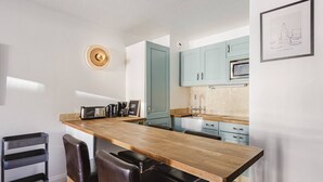 A modern kitchen with a wooden island, black chairs, a coffee machine, and teal cabinets.
