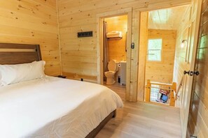 Een houten kamer met een bed, een badkamer met toilet en wastafel, en een klein raam.