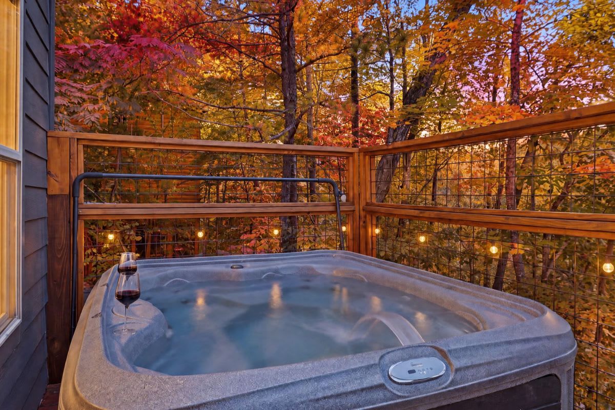 A hot tub with a wooden railing, surrounded by autumn foliage.