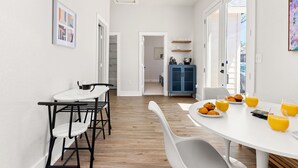 A modern kitchen with a dining area, featuring a white table, chairs, and a breakfast setup with orange juice and pastries. - Stylish Home Nr DT, Alamo, River Walk | Games WiFi (San Antonio)