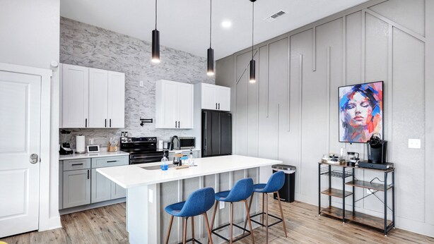 A modern kitchen with white cabinets, a large island with bar stools, and a black refrigerator. - Stylish Home Nr DT, Alamo, River Walk | Games WiFi (San Antonio)