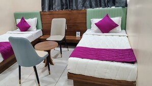 Quarto de hotel com duas camas, uma cadeira e uma mesa pequena.