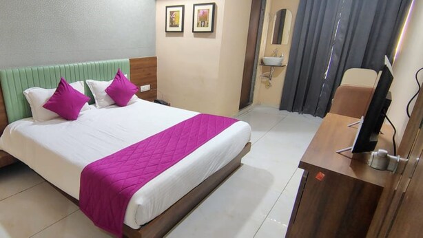 Quarto de hotel com cama, escrivaninha, televisão e banheiro.
