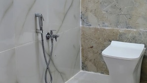Casa de banho com azulejos de mármore branco, sanita branca e chuveiro com flexa.