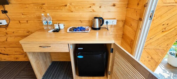 A compact wooden room with a kitchenette, a small refrigerator, a kettle, and a tray of snacks. - The Nine Beach Resort Patnem Goa (Canacona)