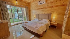 Ein Schlafzimmer einer Holzhütte mit einem großen Bett, einem Deckenventilator, einer Klimaanlage und Blick ins Freie durch eine Schiebetür.