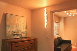 A room with a wooden dresser, a painting of sailboats, and a string of lights on the wall.