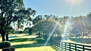 Un campo da golf con una recinzione di legno, alberi e cielo sereno.