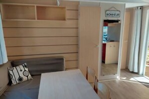 A compact room with a bed, a table, and a bench. There's a door leading to a kitchenette area. - Super Mercure (5 people)   (La Boissière-de-Montaigu)
