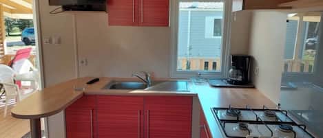 A compact kitchen with a gas stove, a sink, and red cabinets.