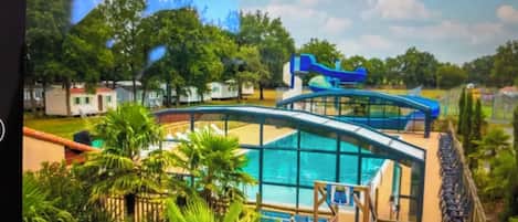 A swimming pool with a slide, surrounded by palm trees and a clear sky.