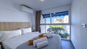 Habitación de hotel con una cama grande, una ventana con vista a edificios y un equipo de aire acondicionado en la pared.