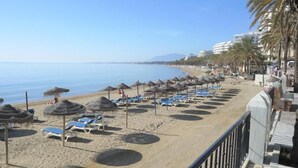 Una playa con tumbonas y sombrillas, cielo despejado y una costa con edificios.