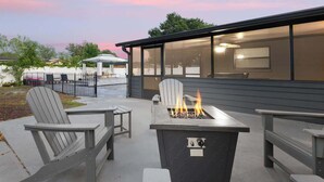 Un patio al aire libre con sillas Adirondack, un brasero y un edificio con amplias ventanas.