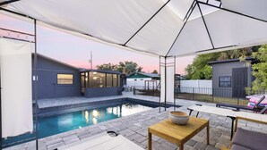 Zona junto a la piscina con un área de descanso cubierta, una pequeña mesa con un cuenco y una piscina.