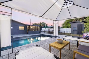 A poolside area with a covered seating area, a small table with a bowl, and a pool.
