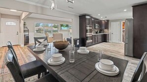 Una cocina moderna con armarios oscuros, una zona de comedor con una mesa grande para cuatro personas y vistas al exterior.