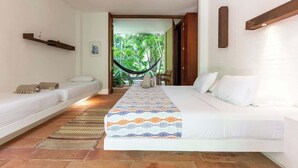 Un dormitorio con dos camas individuales, una cama grande con colcha estampada, una hamaca y vistas a un jardín exuberante.