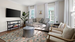 A living room with a sofa, armchair, coffee table, TV, and a patterned rug. - The Moultrie Suite | Walk to Lamar's Sporting Club (Charleston)