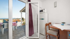 A balcony with a sliding door, a dining table with chairs, a refrigerator, and a view of the sea. - Studio Apartment Anna Vodice (Vodice)