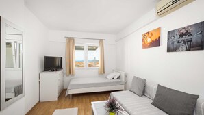 A modern bedroom with a bed, a sofa, a TV, and a window with curtains. - Studio Apartment Anna Vodice (Vodice)