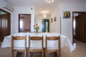 A dining area with a table set for four, wooden chairs, a vase with flowers, and a chandelier.