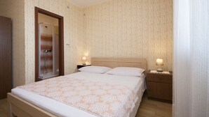 Un dormitorio ordenado con una cama grande, dos mesitas de noche con lámparas, un armario de madera y una puerta que da al baño.