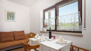 Un comedor con una mesa dispuesta para dos, una silla de madera, un sofá y un ventanal con vistas a la vegetación.