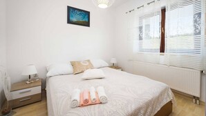 Un dormitorio ordenado con cama, mesitas de noche, lámpara y ventana con cortinas.