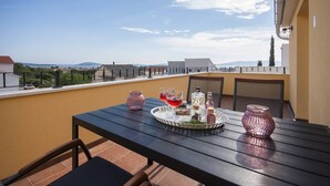 Ein Balkon mit Tisch für zwei Personen, ausgestattet mit einem Tablett, das Getränke und Flaschen, eine Vase und einen Stuhl zeigt.