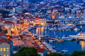 A marina with boats docked, a waterfront promenade, and buildings with red roofs.