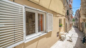 A narrow street with buildings on either side, featuring a window with shutters and a small outdoor seating area with a table and chairs. - Studio Apartment Matija Vodice (Vodice)