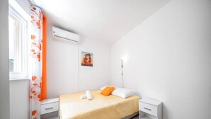 A modern bedroom with a bed, a nightstand, a wall-mounted air conditioner, and a window with orange curtains. - Studio Apartment Matija Vodice (Vodice)