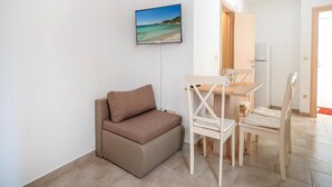A small living room with a sofa, a dining table with chairs, a TV mounted on the wall, and a door leading to another room. - Studio Apartment Matija Vodice (Vodice)