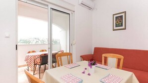 A dining area with a table set for four, chairs, a red sofa, and a sliding glass door leading to an outdoor balcony.